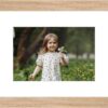 Framed photo of a young girl holding flowers, set in a light wood frame with white matting.