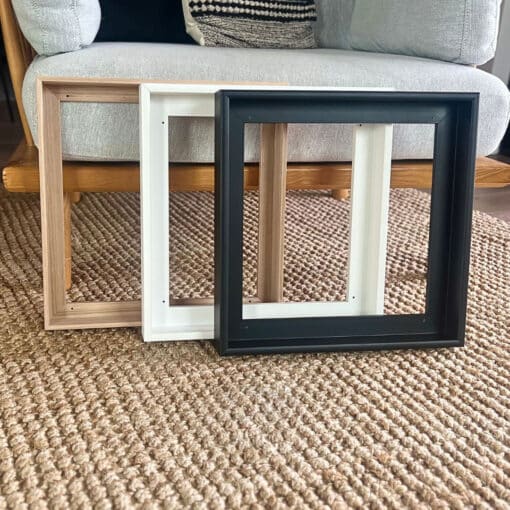 Three empty picture frames in wood, white, and black, resting on a textured rug.
